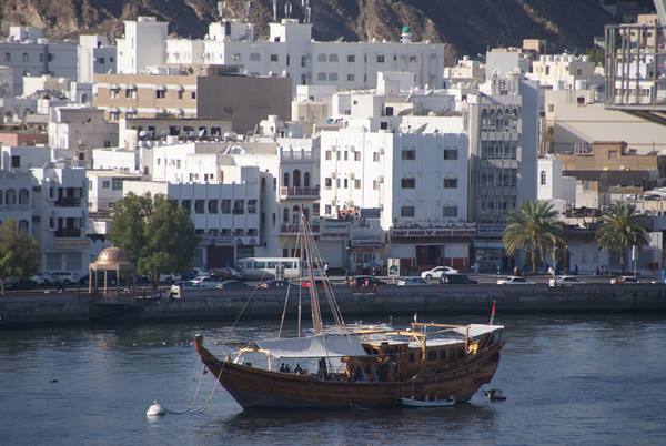 Wooden dhow moored in front of Muscat's white waterfront buildings