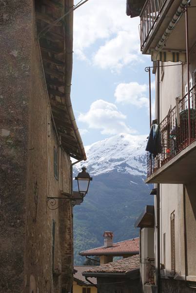 Alley between houses with balconies and lantern, snowy mountain among clouds