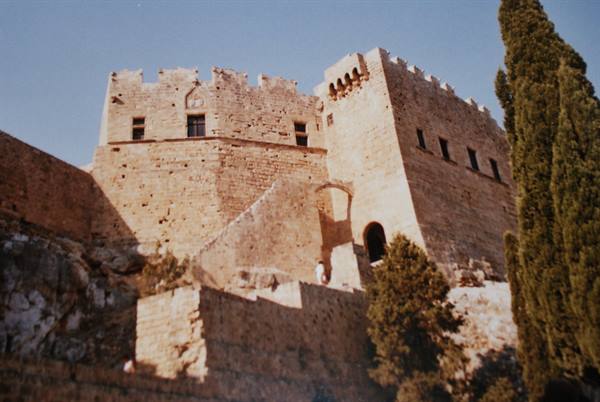 Ancient golden stone fortress on rocks, cypress tree on right, morning light