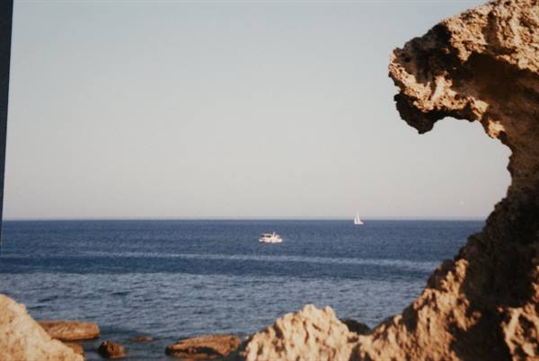 Boat and sailboat on blue sea framed by limestone rock