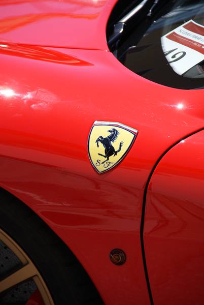 Ferrari badge on a glossy red car fender under sunlight