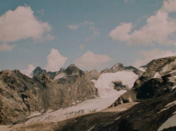 White glacier between grey rocky peaks under clouds in sunlight