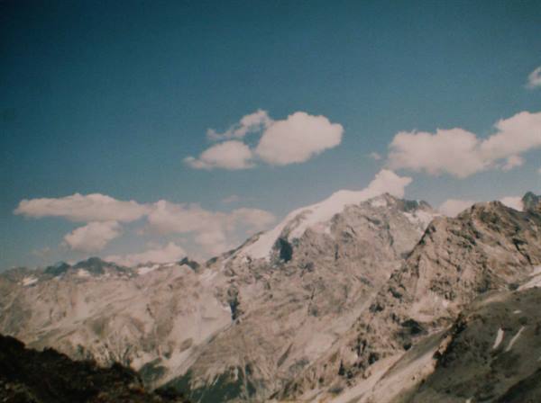 Snow-capped rocky peak beneath white clouds, blue sky, vintage film
