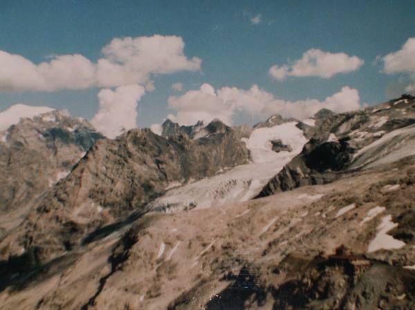 Glacier between snowy rocky peaks, white clouds over blue sky