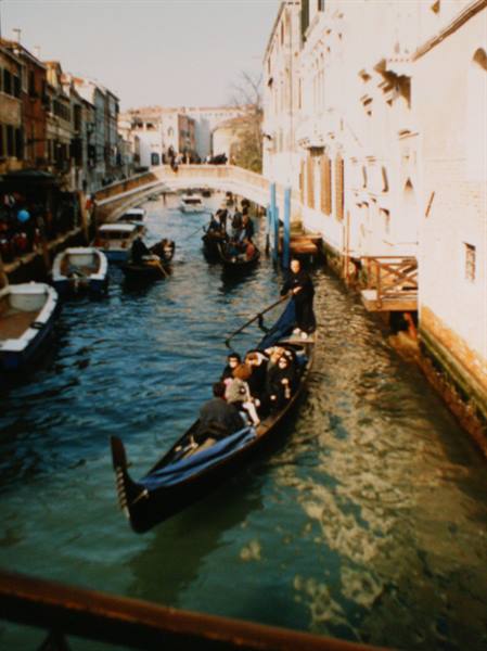 Gondolier carrying tourists on a black gondola along a Venice canal