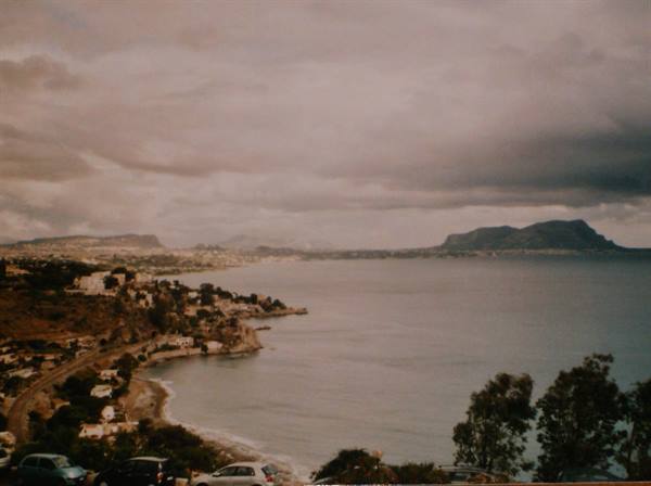 Grey clouds over a bay with white houses on rocky coast, parked cars