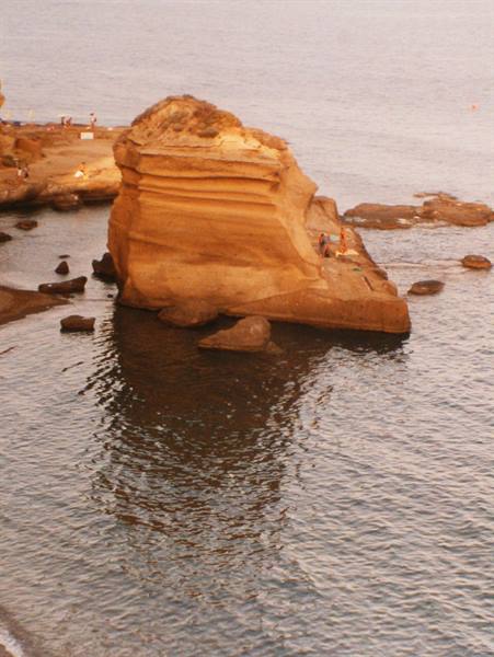 Large yellow tuff rock in calm sea, swimmers sitting on the stone