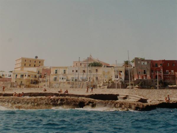 Colorful houses along rocky shore, people on the wall, blue sea