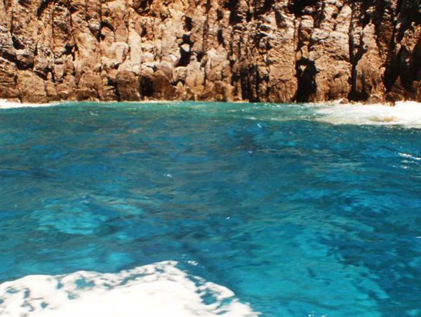 Turquoise water with foam in front of dark volcanic cliffs