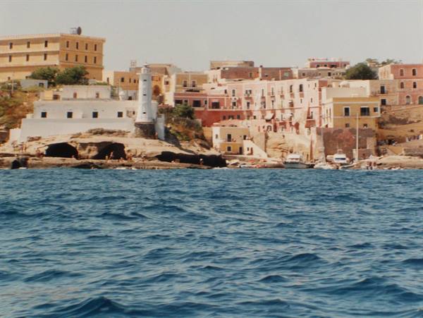 Colored houses and white lighthouse on Ventotene rocky coast, boat on blue sea