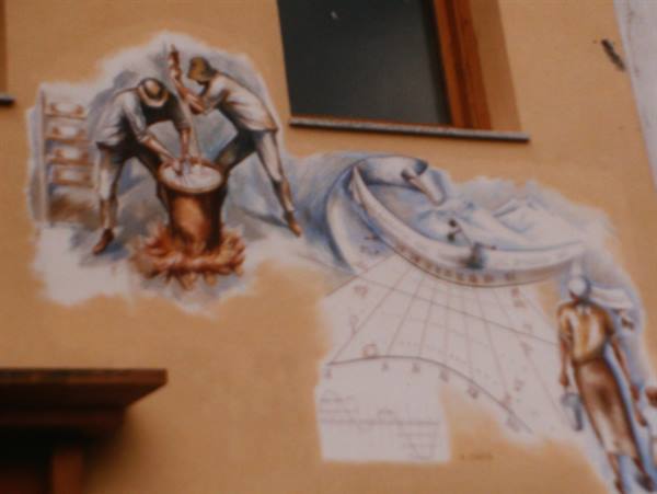 Mural on yellow wall showing blacksmiths working and painted sundial