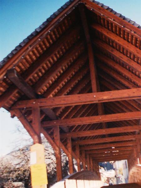 Wooden covered structure with red beams and shingled roof under blue sky