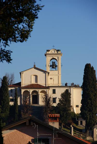 White sanctuary with bell tower and terracotta roofs among cypresses, golden light