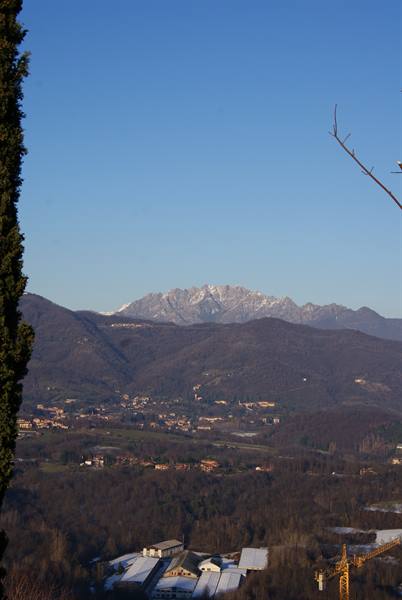 Snowcapped Apuan Alps rise above a valley with houses and a yellow crane