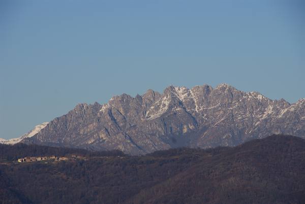 Snow-dusted Resegone peaks rise above wooded hills and distant farmhouses