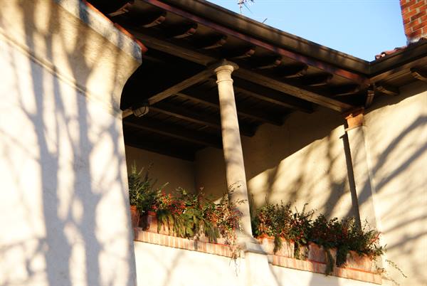 Stone-columned porch with flowers, tree shadows on the wall