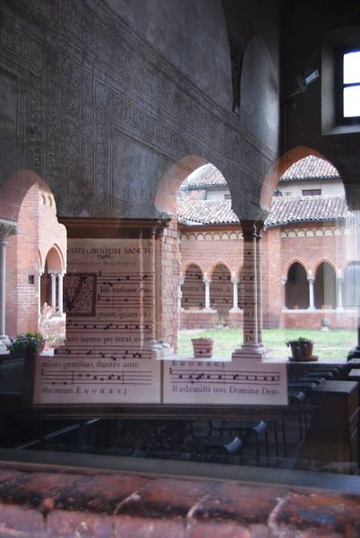 Brick Romanesque cloister with arcades reflected on glass with sheet music
