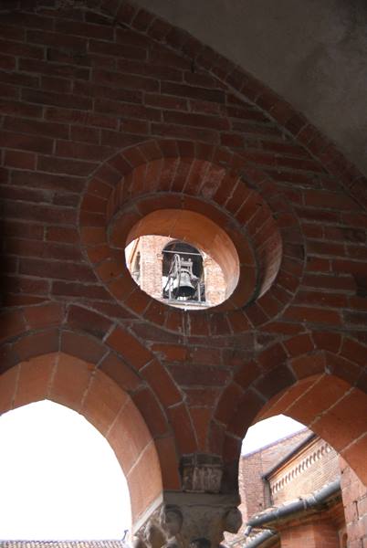 Brick round opening revealing a bell, cloister arches below