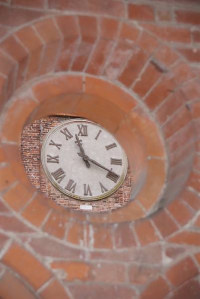 Clock face with roman numerals framed by a red brick oculus