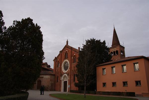 Brick church with rose window and bell tower, grey sky, two people walking