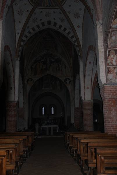 Medieval church interior with frescoes, cross vaults, brick pillars and wooden pews