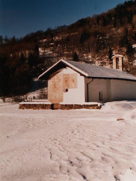 Small white church with frescoes and bell tower, snowy woods behind