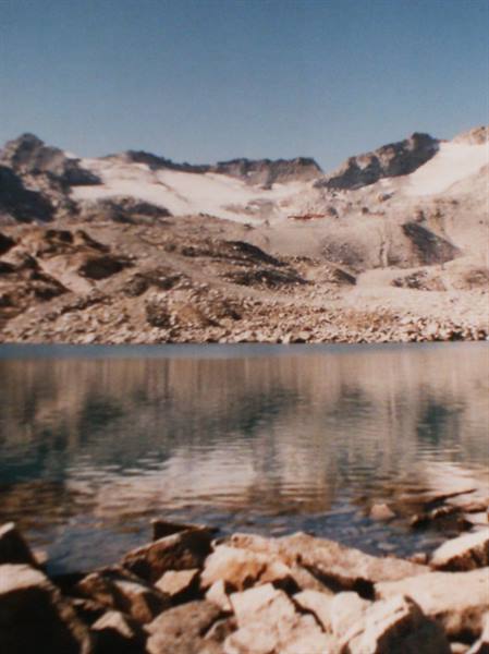 Alpine lake with calm water, foreground rocks and reflected rocky peaks