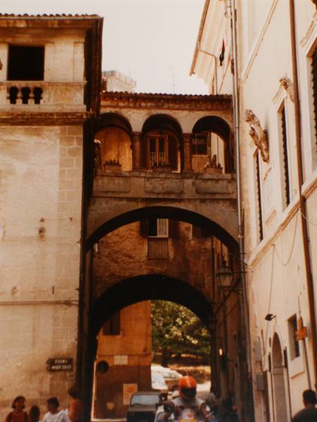 Medieval stone arch over the street, people and a scooter passing