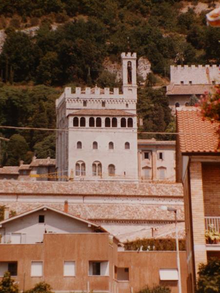 Palazzo dei Consoli in Gubbio rising above tiled roofs, stone tower against wooded hill