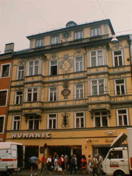 Yellow ornate building with Humanic shop sign, pedestrians and vans on the street