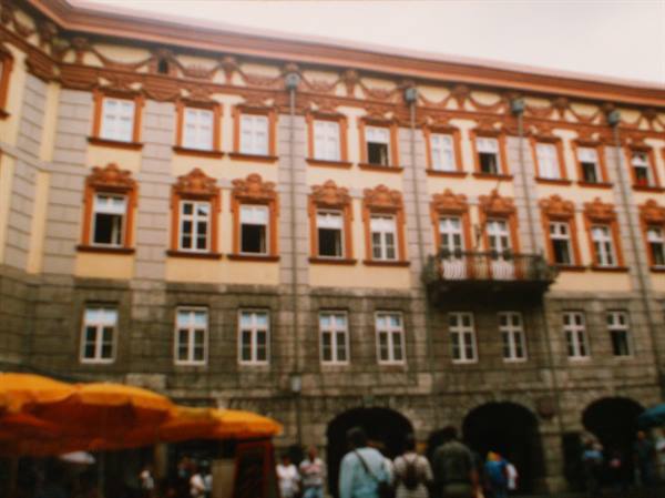 Ochre building with orange stucco, yellow umbrellas, blurred passersby on the square