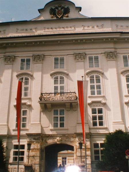 White baroque facade with golden double-headed eagle, wrought-iron balcony, red banners