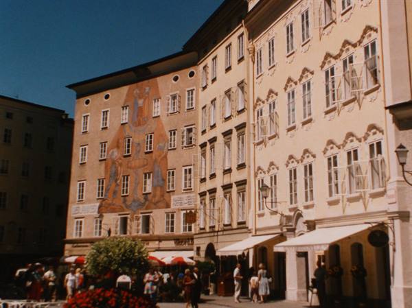Tourists stroll past an ochre building with large fresco, Salzburg