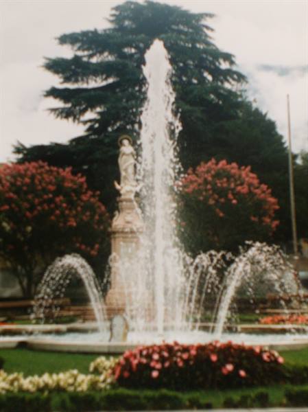 Fountain with water jets and statue among flowers and conifer in park