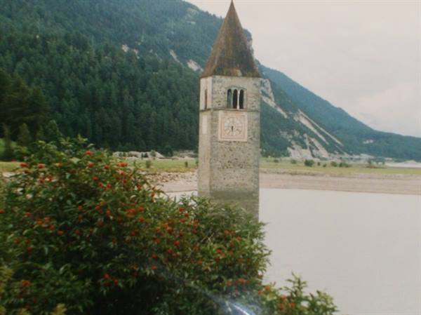 Stone bell tower half-submerged in Lake Resia, surrounded by forested mountains