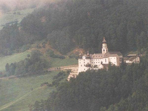 White monastery with tower among forests and green meadows in mist