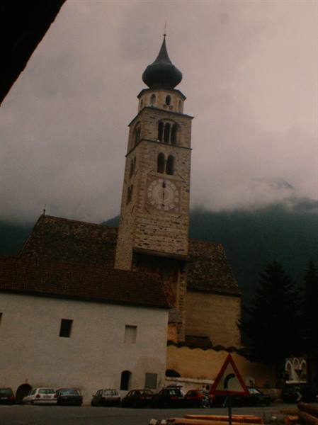 Stone bell tower with black onion dome and clock, cars parked below