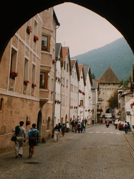 Medieval arch over cobblestone street with painted houses, Sterzing