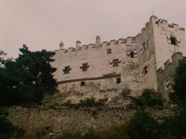 White castle with battlements and red eagle emblems, surrounded by trees
