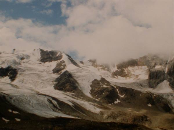 Snowy glacier between rocky walls, low clouds covering the peaks