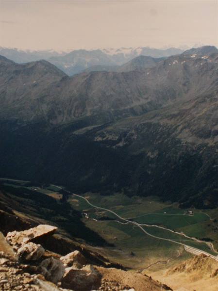 Road winding through green valley among rocky mountains and snowy peaks