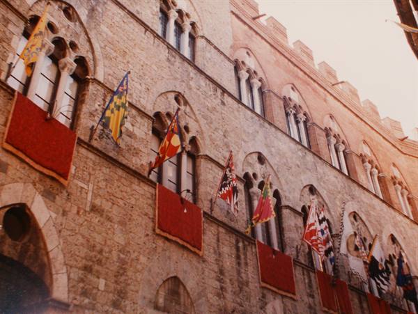 Siena's medieval brick facade with red drapes and Palio banners