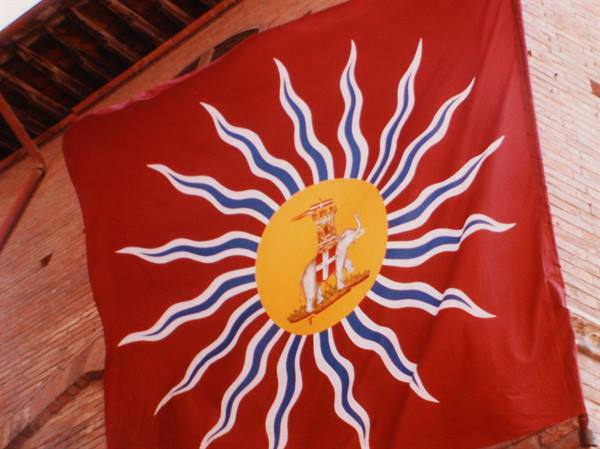 Red flag with radiating sun and elephant, hanging against bricks under a roof