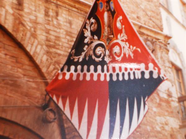 Red and black heraldic banner hanging on a Siena brick facade