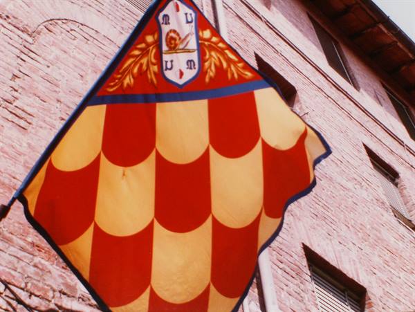 Red and yellow contrada banner with crest against Siena's brick wall