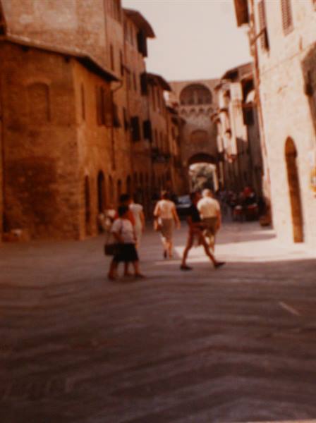 Tourists crossing a brick medieval street lined with old stone houses