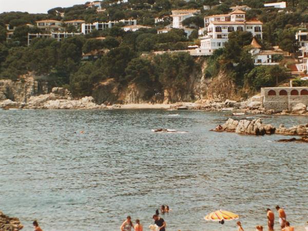 Swimmers with yellow parasol on beach below houses among pines, Costa Brava
