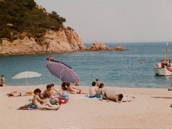 Beachgoers under umbrellas on the sand, boat moored near the rocks