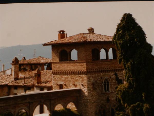 Brick tower with arches and terracotta roofs, cypress beside it