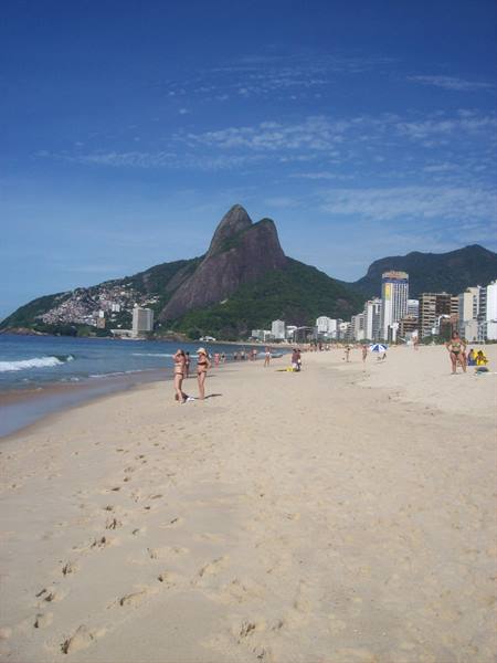 Beachgoers walk on Ipanema sand with high-rises and Morro Dois Irmãos
